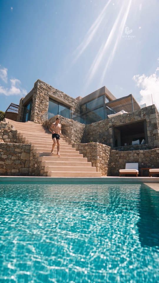 Vivienda de piedra y vidrio sobre una piscina, con una escalera exterior